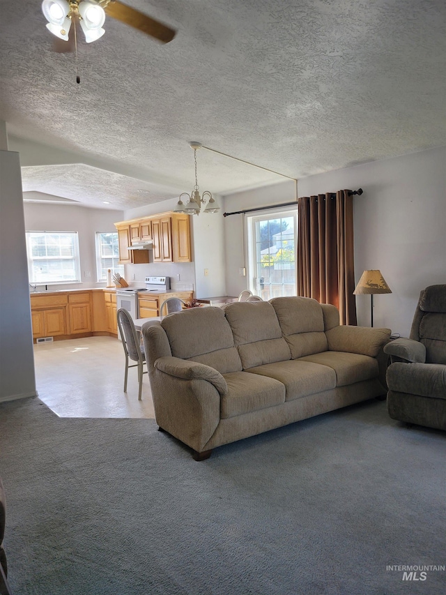 carpeted living room featuring a textured ceiling, ceiling fan with notable chandelier, plenty of natural light, and vaulted ceiling