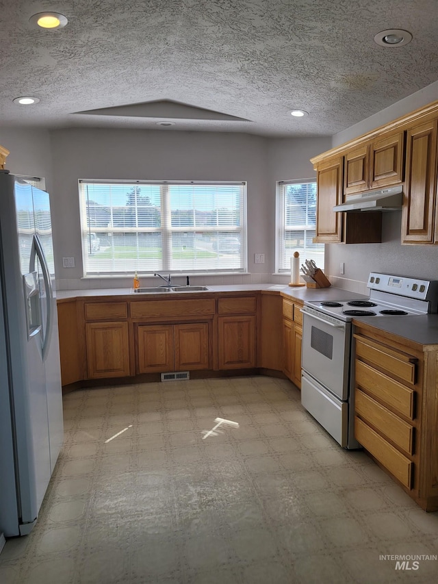 kitchen featuring white fridge with ice dispenser, stove, sink, and a textured ceiling