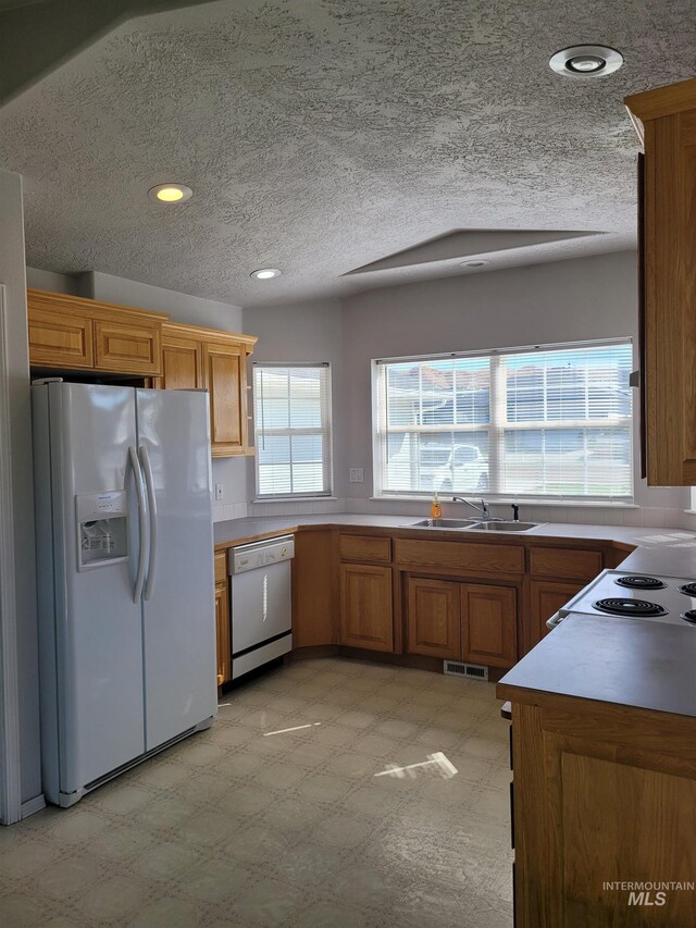 kitchen featuring lofted ceiling, white appliances, a textured ceiling, and sink