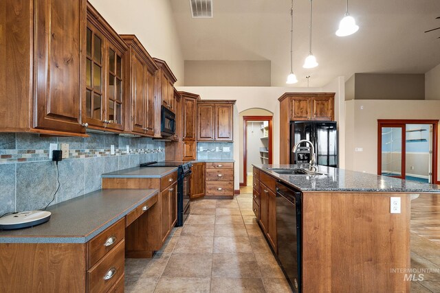 kitchen with visible vents, an island with sink, arched walkways, black appliances, and a sink