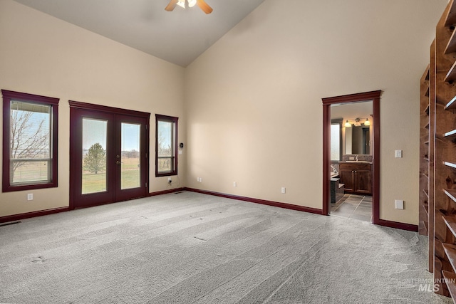 carpeted spare room featuring french doors, high vaulted ceiling, baseboards, and a ceiling fan