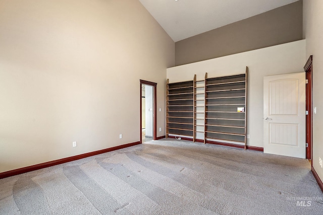 carpeted spare room featuring baseboards and high vaulted ceiling