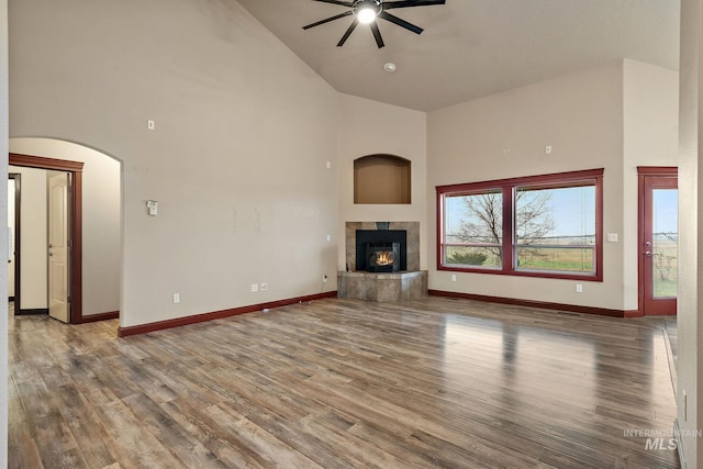 unfurnished living room with wood finished floors, a fireplace, baseboards, and high vaulted ceiling