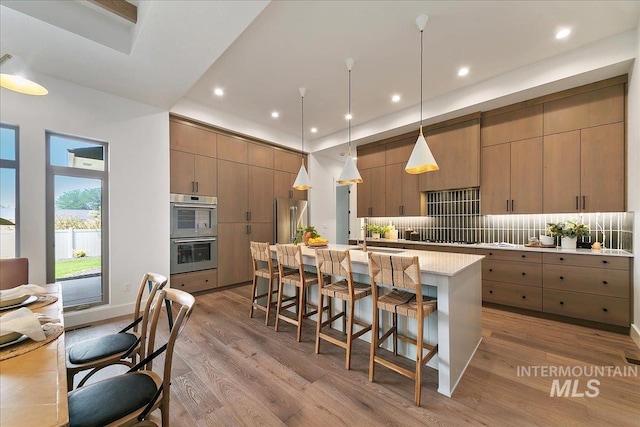 kitchen with stainless steel appliances, backsplash, pendant lighting, light hardwood / wood-style floors, and a center island with sink