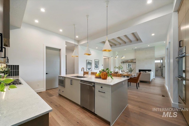 kitchen with a kitchen island with sink, white cabinets, decorative light fixtures, a large fireplace, and stainless steel appliances