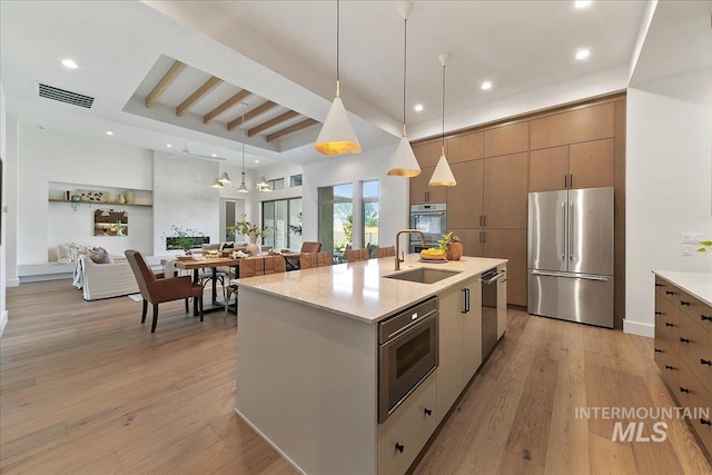 kitchen with sink, light stone countertops, an island with sink, appliances with stainless steel finishes, and decorative light fixtures