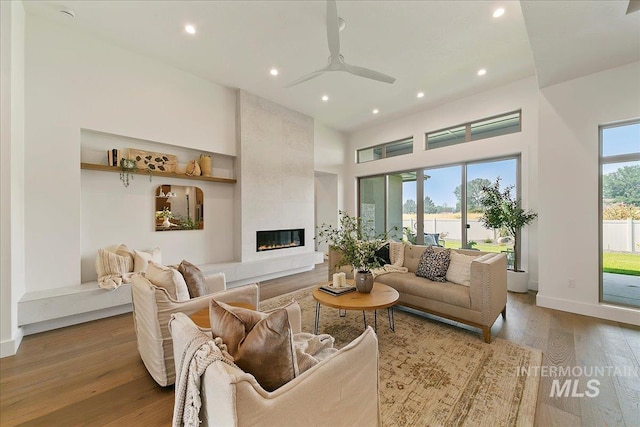 living room with a fireplace, light wood-type flooring, a wealth of natural light, and ceiling fan