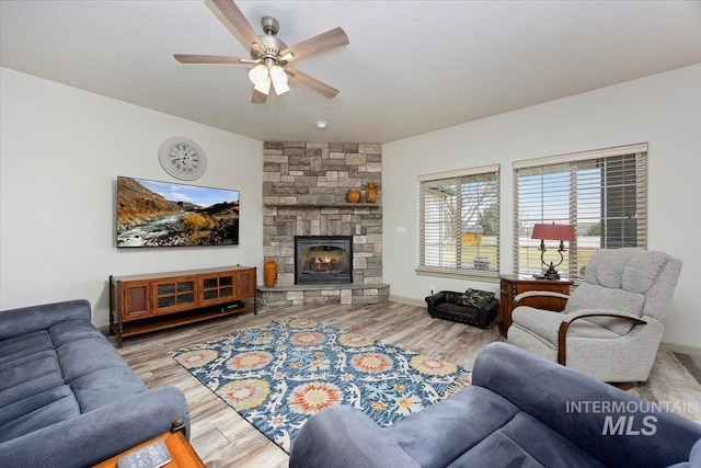 living room featuring ceiling fan, a stone fireplace, and wood-type flooring