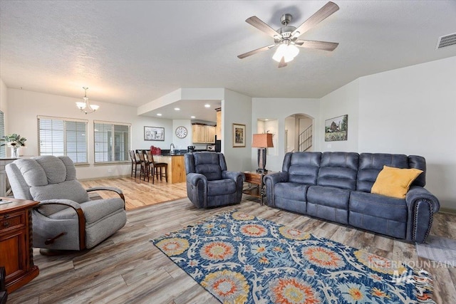 living room with ceiling fan with notable chandelier, wood-type flooring, and a textured ceiling