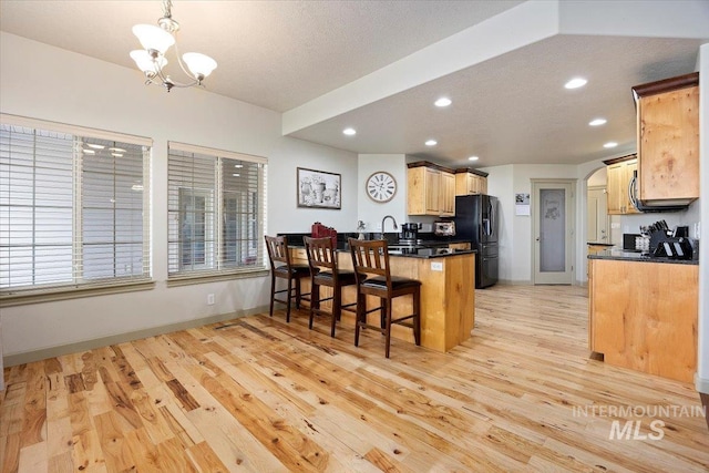 kitchen featuring light hardwood / wood-style floors, hanging light fixtures, kitchen peninsula, a notable chandelier, and black fridge