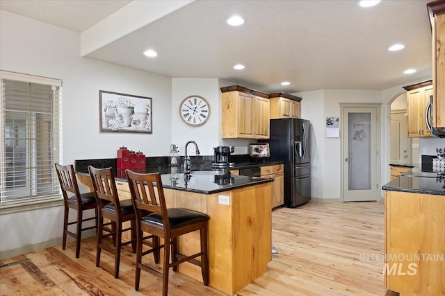 kitchen featuring kitchen peninsula, black fridge with ice dispenser, light hardwood / wood-style flooring, a kitchen bar, and sink