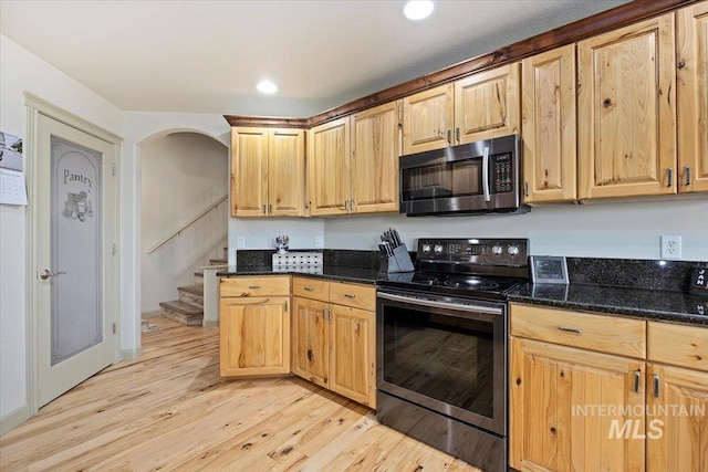 kitchen featuring appliances with stainless steel finishes, light hardwood / wood-style floors, and dark stone countertops