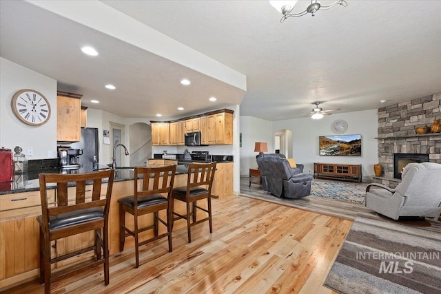 interior space with electric range, a stone fireplace, light hardwood / wood-style floors, sink, and ceiling fan with notable chandelier