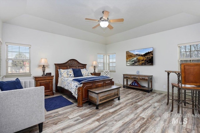 bedroom with a raised ceiling, ceiling fan, multiple windows, and light wood-type flooring