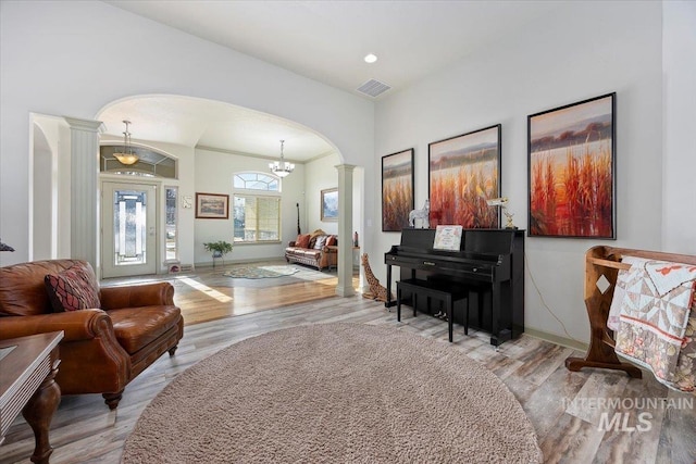 living area featuring decorative columns, light wood-type flooring, and a notable chandelier