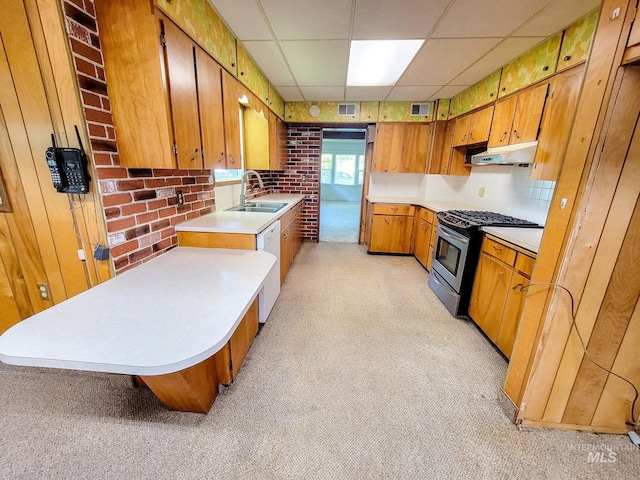 kitchen featuring sink, gas stove, light colored carpet, a drop ceiling, and brick wall