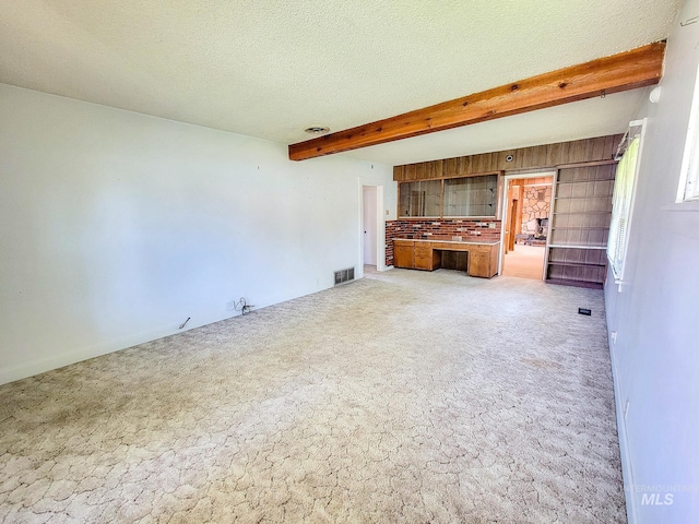 unfurnished living room with a textured ceiling, light carpet, and beam ceiling