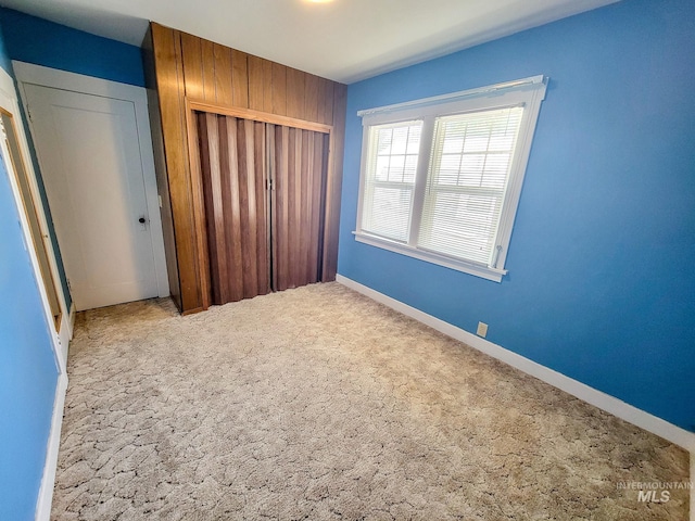 unfurnished bedroom featuring carpet flooring, wood walls, and a closet