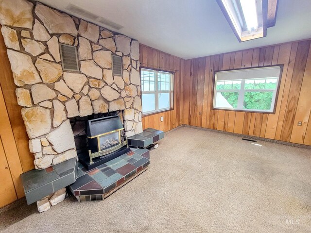 living room featuring a fireplace, a wood stove, wood walls, and carpet