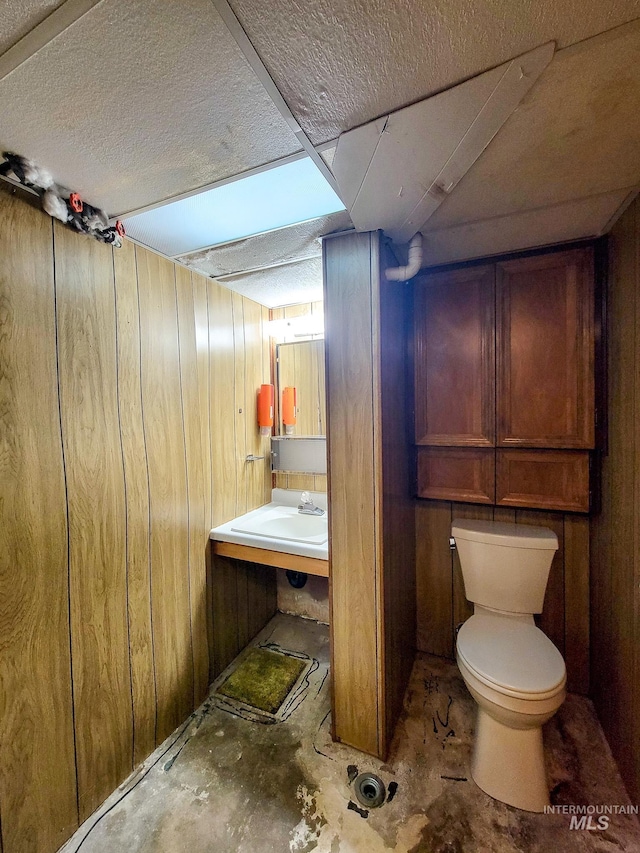 bathroom with wood walls, sink, and toilet