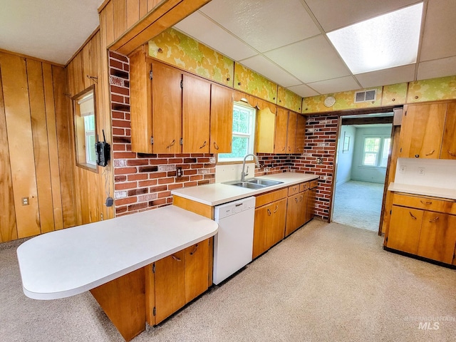 kitchen with sink, dishwasher, light colored carpet, a paneled ceiling, and wood walls