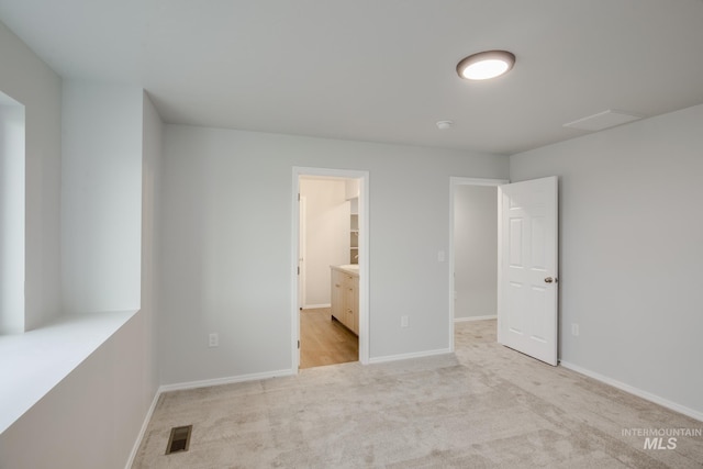 unfurnished bedroom featuring visible vents, ensuite bath, light colored carpet, and baseboards