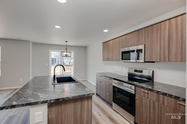 kitchen featuring sink, a center island with sink, light hardwood / wood-style flooring, appliances with stainless steel finishes, and a notable chandelier