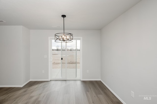unfurnished dining area with visible vents, a chandelier, wood finished floors, and baseboards