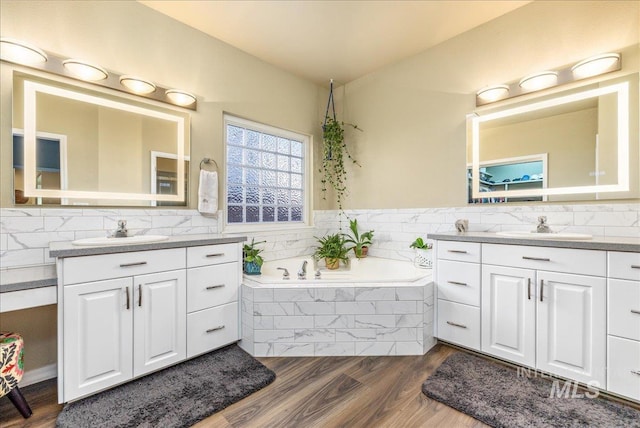 bathroom featuring hardwood / wood-style flooring, a relaxing tiled tub, and vanity