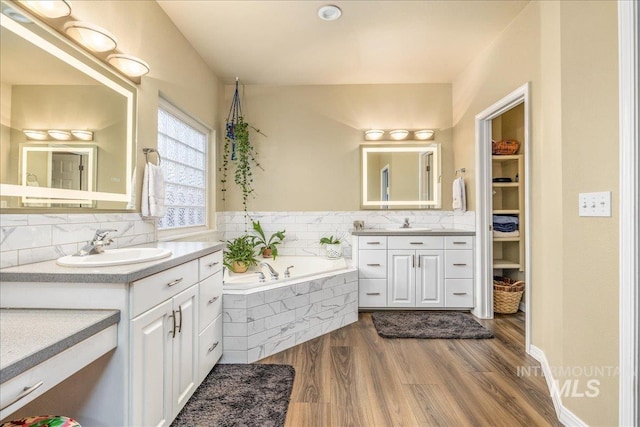 bathroom with wood-type flooring, vanity, and a relaxing tiled tub