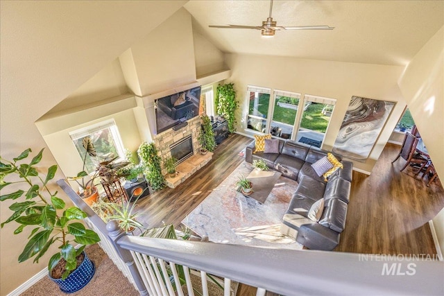 living room with a wealth of natural light, high vaulted ceiling, a stone fireplace, and ceiling fan