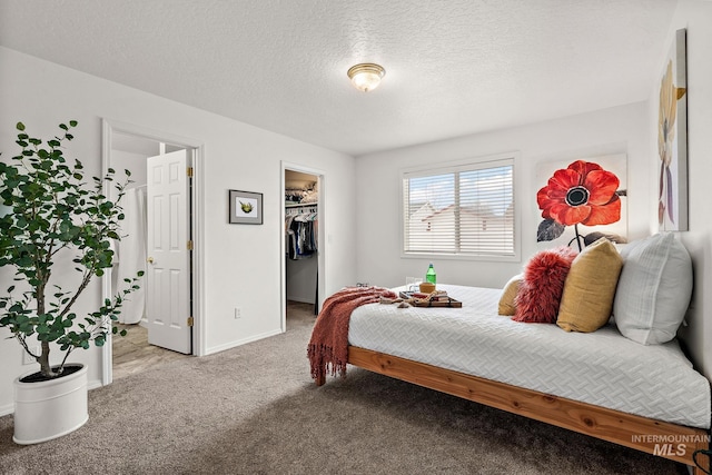 bedroom with a spacious closet, a closet, a textured ceiling, and carpet