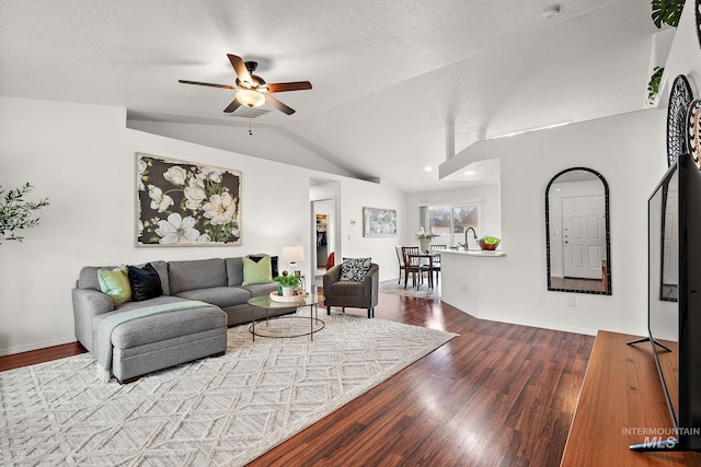 living room featuring wood-type flooring, lofted ceiling, ceiling fan, and a textured ceiling