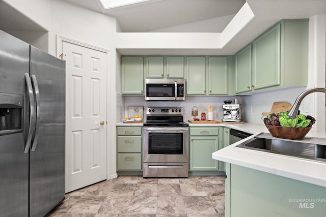 kitchen with sink, appliances with stainless steel finishes, a tray ceiling, green cabinets, and decorative backsplash