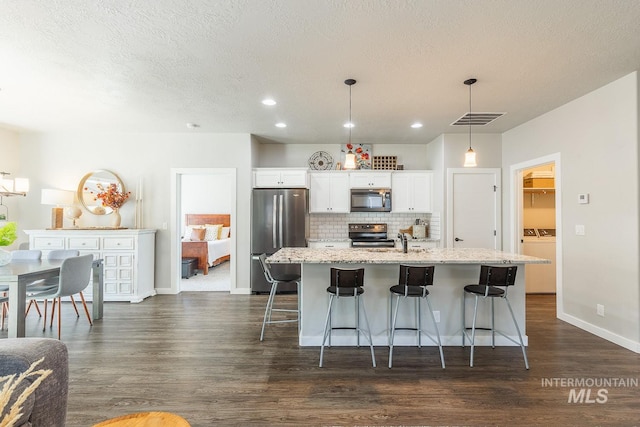 kitchen featuring a breakfast bar area, an island with sink, white cabinetry, appliances with stainless steel finishes, and decorative light fixtures