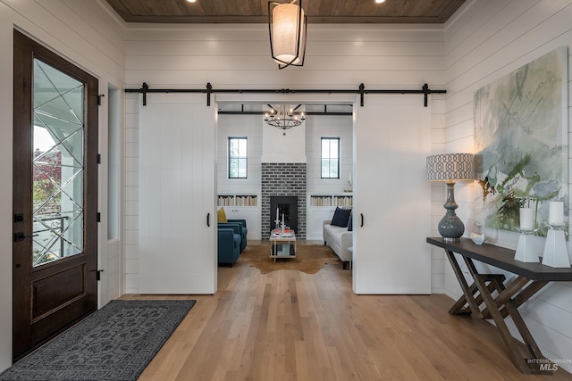 entrance foyer with light hardwood / wood-style floors, wood ceiling, a brick fireplace, a chandelier, and a barn door