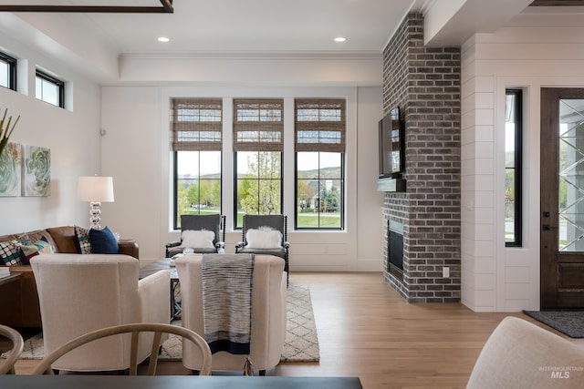 living room with light wood-type flooring, a brick fireplace, and ornamental molding