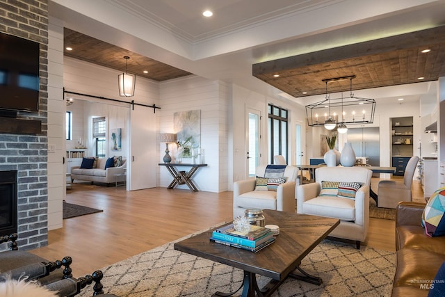 living room featuring a barn door, an inviting chandelier, light hardwood / wood-style floors, and a brick fireplace