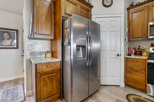 kitchen featuring light stone countertops, stainless steel appliances, and light wood-type flooring