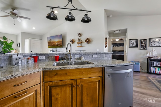 kitchen with light stone counters, wood-type flooring, vaulted ceiling, dishwasher, and sink