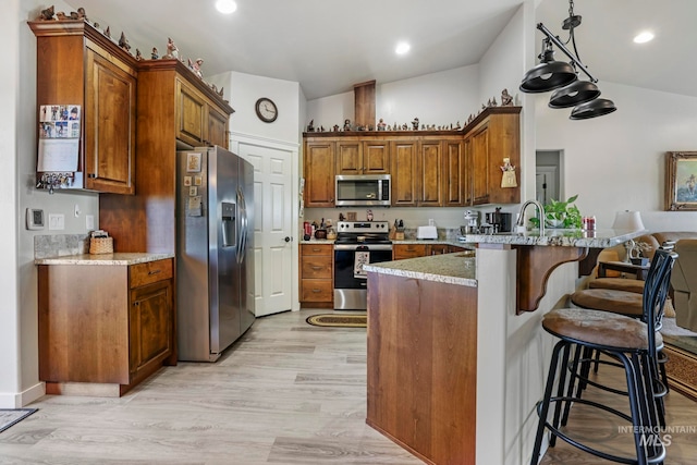 kitchen with light stone counters, a kitchen breakfast bar, light wood-type flooring, vaulted ceiling, and stainless steel appliances