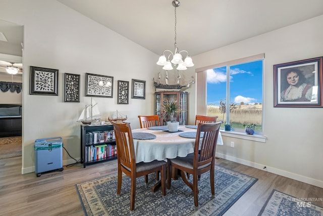 dining space with hardwood / wood-style floors, ceiling fan with notable chandelier, and vaulted ceiling