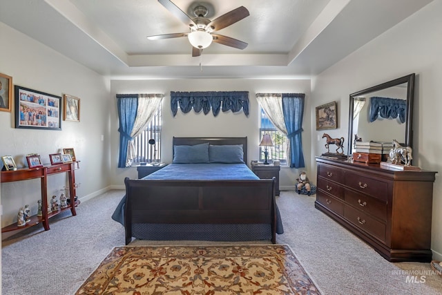 bedroom with light colored carpet, a tray ceiling, and ceiling fan