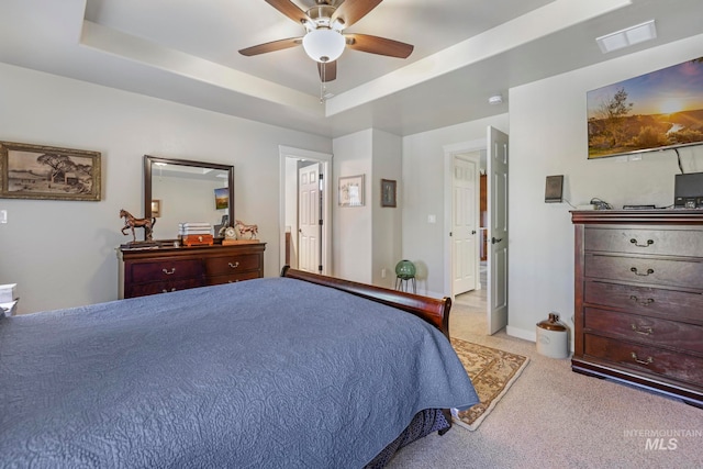 carpeted bedroom with a raised ceiling and ceiling fan