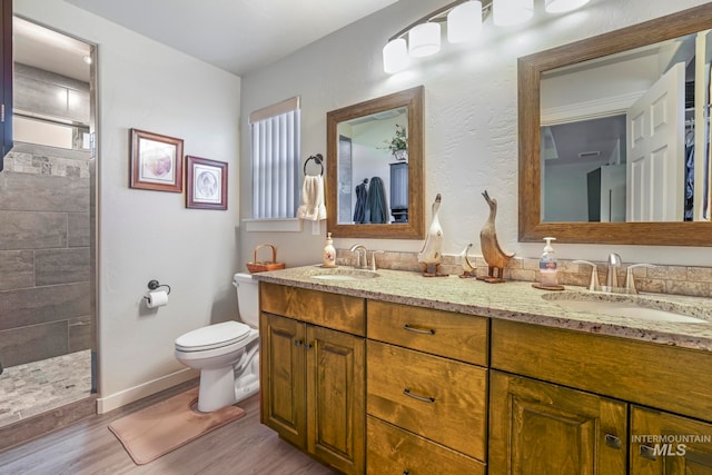 bathroom featuring toilet, hardwood / wood-style flooring, vanity, and a tile shower