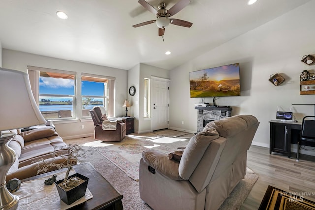 living room featuring ceiling fan, a stone fireplace, vaulted ceiling, and light wood-type flooring