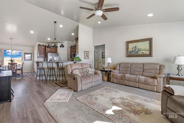 living room with high vaulted ceiling, ceiling fan with notable chandelier, and light wood-type flooring