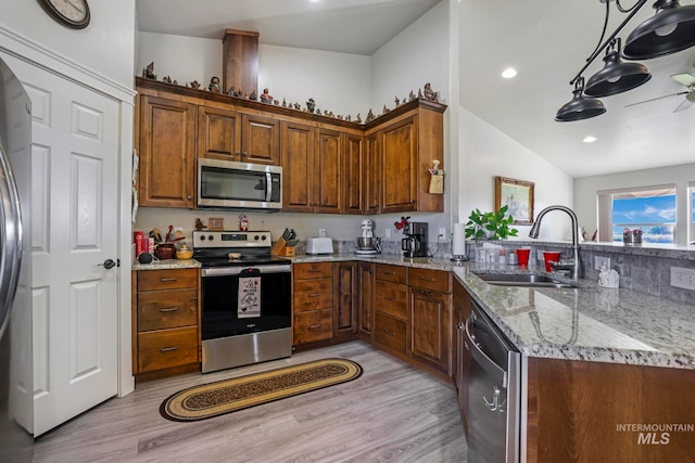 kitchen with light stone counters, light hardwood / wood-style flooring, sink, pendant lighting, and stainless steel appliances