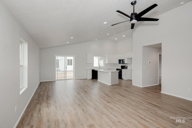 unfurnished living room featuring ceiling fan, a textured ceiling, high vaulted ceiling, and light hardwood / wood-style flooring