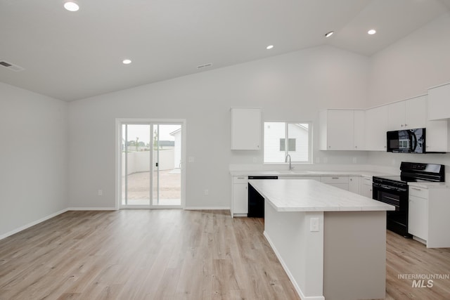 kitchen with sink, a kitchen island, light hardwood / wood-style floors, white cabinets, and black appliances